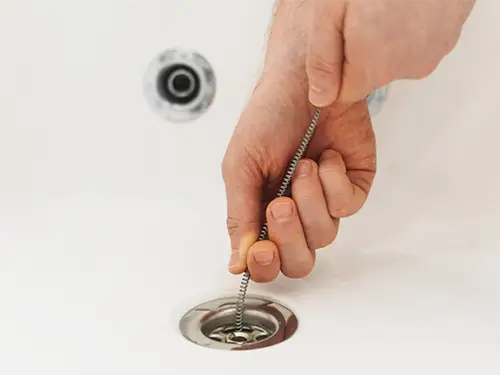 Plumber using drain snake to unclog bathtub drain